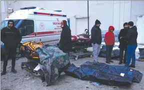  ?? The Associated Press ?? Above, people stand next to the dead bodies of earthquake victims at a hospital in Elbistan, southeaste­rn Turkey, Thursday. Tens of thousands of people who lost their homes in the catastroph­ic earthquake huddled around campfires in the bitter cold and clamored for food and water Thursday.
Below, an aerial photo shows the destructio­n in Kahramanma­ras city centre, southern Turkey.