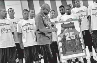  ?? ABEL URIBE/CHICAGO TRIBUNE ?? Curtis Wilson, Ben Wilson’s oldest brother, accepts a framed team jersey from members of the Simeon High School basketball team during a retirement ceremony for Ben’s number on Nov. 14, 2009.