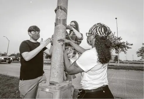  ?? Steve Gonzales / Staff photograph­er ?? J.C. Yordy, from left, his sister, Kate, and Natile Farris tie ribbons along Cullen Boulevard in Pearland to mark George Floyd’s funeral route. The show of sympathy was organized online by a group of Pearland mothers saddened by Floyd’s last words calling for his mom.