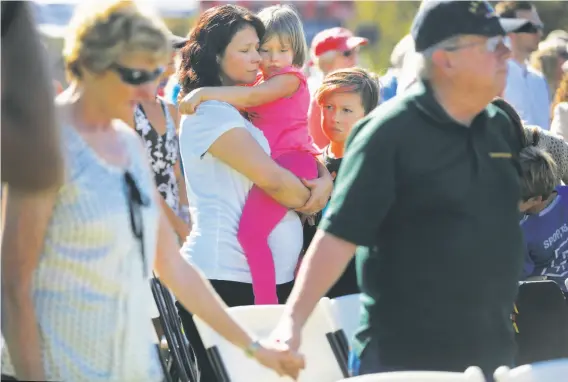  ?? Photos by Leah Millis / The Chronicle ?? Esmeralda Bishop holds daughter Alyssa, 5, as son Brandon, 10, stands next to her while a bell is rung for every life lost in the Wine Country wildfires.