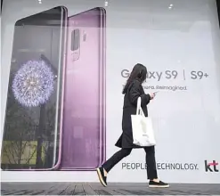  ?? —AFP ?? SEOUL: In this file photo taken on April 05, 2018 a woman walks past an advertisem­ent for the Samsung Galaxy S9 at a mobile phone shop.