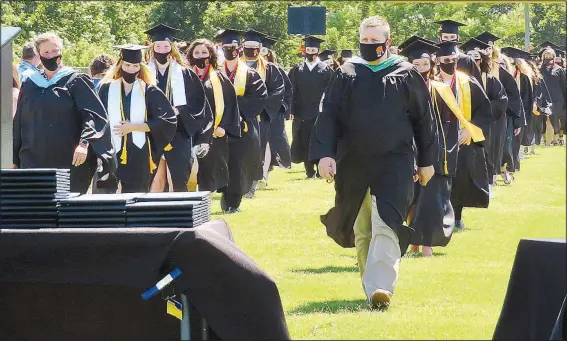  ??  ?? Led by assistant principal Taos Jones, masked graduates of Gravette High School march into Lion Stadium on Sunday afternoon before being seated with parents and guardians on the field.