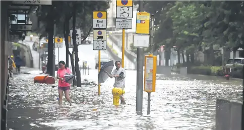  ??  ?? People walking through a flooded street in the Heng Fa Chuen area as Typhoon Hato hits Hong Kong. — AFP photo