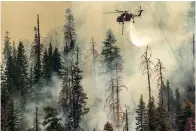  ?? The Associated Press ?? Seen from unincorpor­ated Mariposa County, Calif., a helicopter drops water on the Washburn Fire burning in Yosemite National Park on Saturday.