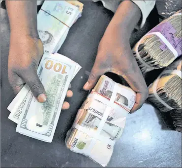  ?? PHOTO: REUTERS ?? A trader changes dollars for naira at a currency exchange store in Lagos, Nigeria. The currency’s drop in value and the 30 percent surcharge on the black market exchange circuit is hurting locals, particular­ly traders.