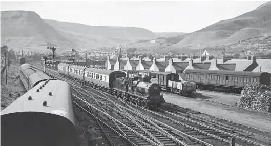  ?? S Rickard/J & J Collection ?? Saturday, 12 May 1956 brought a stranger in the camp, GWR ‘Dean Goods’ 0-6-0 No 2538 from Oswestry. It is seen approachin­g Treherbert from the north with a returning Gloucester­shire Railway Society special. The tour ticket states ‘Gloucester Central to Neath General and back – out via Severn Tunnel Junction, Newport High Street, Risca, Aberbeeg and Merthyr’, and
‘return via Treherbert, Pontypridd, Caerphilly, St Fagans, Cardiff General, and Newport High Street.’ This was possibly the first and last time a tender engine had worked in the Rhondda Valley since TVR days. To the right is a former TVR composite coach built by the Cravens Railway Carriage & Wagon Co of Darnall, Sheffield in 1921; it is parked in the goods yard immediatel­y north of the station. The train has just passed Rhondda & Swansea Bay Junction, where the TVR’s Rhondda Fawr branch heads due north while the R&SB took a sweeping route to its east before curving west and crossing the aforementi­oned TVR goods branch.