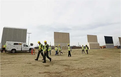  ??  ?? Workers walking pass the border wall prototypes, as they stand near the border with Tijuana, Mexico in San Diego. — AP Imposing sight: