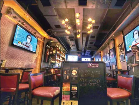  ?? EDMOND TANG / CHINA DAILY ?? An employee talks on his phone at an empty bar in Tsim Sha Tsui on Thursday as television­s air the government announceme­nt of a shutdown of all bars in the city for two weeks from today to contain the pandemic.
