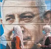  ?? ARIEL SCHALIT/AP ?? Women in face masks walk past a poster of Israeli Prime Minister Benjamin Netanyahu on Sunday in Jerusalem.