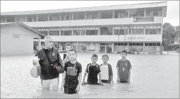  ??  ?? Teachers and students wading in the flood waters. — Bernama photo