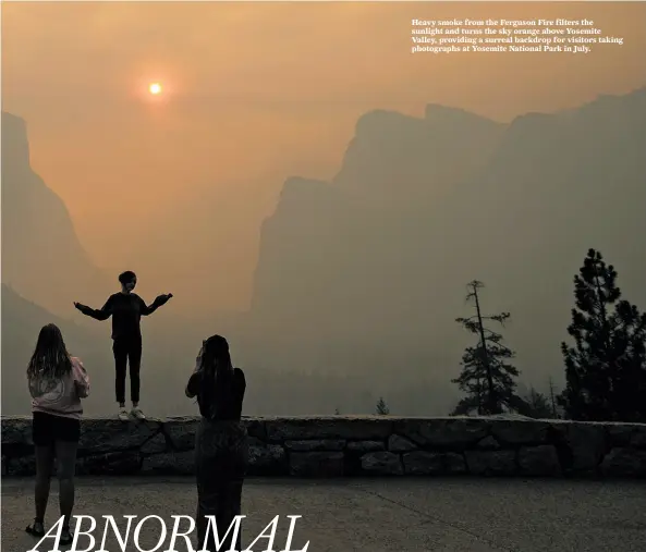  ?? Noah Berger / Associated Press 2018 ?? Heavy smoke from the Ferguson Fire filters the sunlight and turns the sky orange above Yosemite Valley, providing a surreal backdrop for visitors taking photograph­s at Yosemite National Park in July.