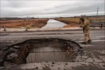  ?? Rodrigo Abd / Associated Press ?? A Ukrainian soldier looks at a damaged bridge Saturday in Bucha, on the outskirts of Kyiv, Ukraine. As Russian forces pull back from Ukraine’s capital region, retreating troops are creating a “catastroph­ic" situation for civilians by leaving mines around homes, abandoned equipment and “even the bodies of those killed."