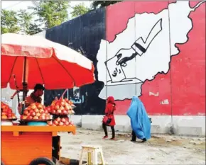  ?? SAJJAD HUSSAIN/AFP ?? An Afghan juice vendor waits for customers next to a mural urging people to vote in Kabul after the first round of Afghanista­n’s national elections.