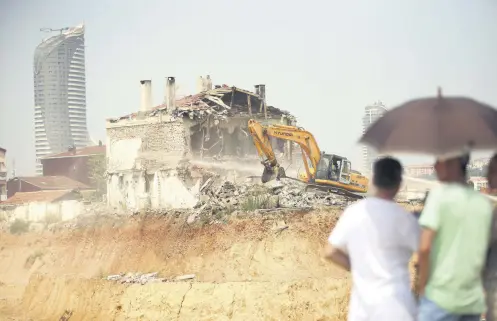  ??  ?? People watch as a bulldozer demolishes a house in Fikirtepe, the Istanbul district where old buildings are being replaced with modern residences as part of urban transforma­tion project.