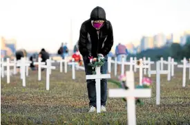  ?? —AFP ?? MEMORIAL A woman places flowers on a cross in honor of those who died of COVID-19. She was part of a demonstrat­ion in Brasilia on Sunday.