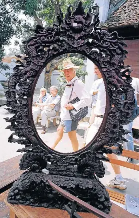  ??  ?? OH, IT’S ME: A tourist takes a quizzical look at himself in an ornate woodenfram­ed mirror at a handicraft bazaar at Hanoi’s Temple of Literature
