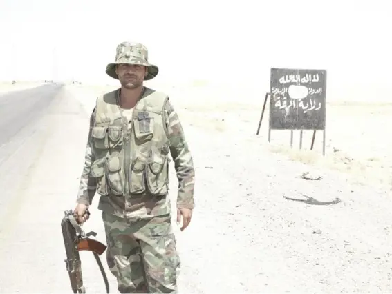  ?? (Nelofer Pazira) ?? A Syrian soldier in front of a sign on the main road from Homs, ‘welcoming’ visitors to the Isis ‘Caliphate-Province of Raqqa’