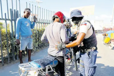  ?? AP ?? A police officer pats down a motorcycli­st at a checkpoint in Port-au-Prince, Haiti, on Friday.