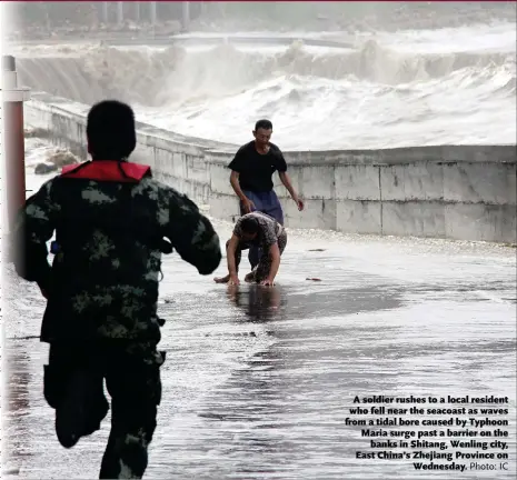  ?? Photo: IC ?? A soldier rushes to a local resident who fell near the seacoast as waves from a tidal bore caused by Typhoon Maria surge past a barrier on the banks in Shitang, Wenling city, East China’s Zhejiang Province on Wednesday.