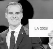  ?? FABRICE COFFRINI/AFP/GETTY IMAGES ?? L.A. mayor Eric Garcetti gets emotional as he holds a card with the designatio­n of LA 2028 after the approving vote.