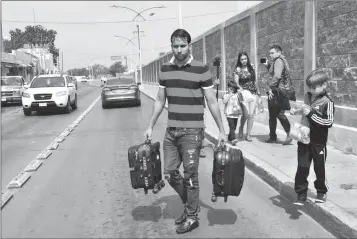  ?? ASSOCIATED PRESS ?? THE ASCENCIO FAMILY, FROM VENEZUELA, CARRY THEIR LUGGAGE after being returned by U.S. authoritie­s to Nuevo Laredo, Mexico on Tuesday as part of the first group of migrants to be sent back to Tamaulipas state under the so-called Remain in Mexico program for U.S. asylum seekers. Approximat­ely 10 migrants crossed the border Monday to seek U.S. asylum and were sent back on Tuesday to wait as their applicatio­ns are processed.