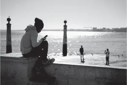  ?? ARMANDO FRANCA AP ?? A teenager checks his cellphone in front of the Tagus River in Lisbon, Portugal, in January.
