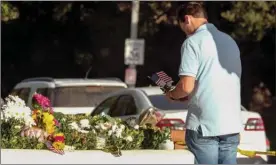  ?? The Associated Press ?? Brian White places a U.S. flag with a flower near the scene of a mass shooting after a gunman opened fire Wednesday evening inside a country music bar, killing multiple people including a responding sheriff’s sergeant.