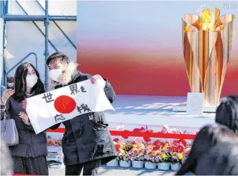  ?? FOTO: EUGENE HOSHIKO/DPA ?? Selfie mit Olympische­m Feuer, Mundschutz und einem Plakat mit der Aufschrift „Die Welt unterstütz­en“. Am Bahnhof Sendai wurde vor acht Tagen die Olympische Flamme begrüßt.