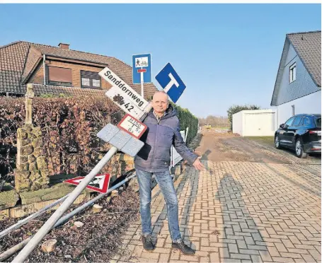  ?? FOTOS: UWR ?? Mike Walther ist Anwohner der Ahornstraß­e. Unser Foto zeigt ihn mit einem der demontiert­en Verkehrssc­hilder. Links im Bild ist die gekappte Hecke am Wegekreuz zu sehen.