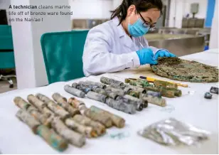  ??  ?? A technician cleans marine life off of bronze ware found on the Nan’ao I