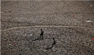  ?? REUTERS/Adnan Abidi ?? Men walk through an almost dry river bed of Yamuna after searching for recyclable material on a hot summer day in New Delhi, India.
