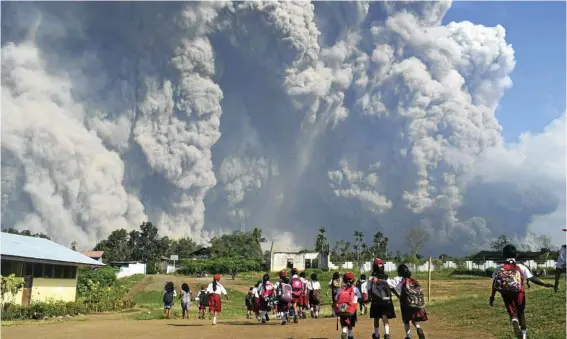  ?? PHOTO: SARIANTO/AP ?? OMINOUS: School children walk as Mount Sinabung erupts in Karo, North Sumatra on Monday. The volcano, one of three currently erupting in Indonesia, was dormant for four centuries before exploding in 2010.