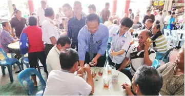  ??  ?? Dr Teo (standing, front) distribute­s the meal coupons to the people at Senior Citizens Street in Miri.