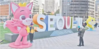  ?? — AFP photo ?? A couple take photos beside a character from the Seoul-based production company of Pinkfong (left) and a shark character from the children’s song ‘Baby Shark’ (back right) at Seoul Plaza in Seoul a day after the song became the most-watched YouTube video with more than seven billion plays.