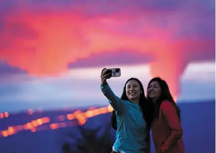  ?? — AP ?? Wonder of nature: Ingrid Yang (left) and Kelly Bruno, both of San Diego, take a photo in front of lava erupting from Hawaii’s Mauna Loa volcano.