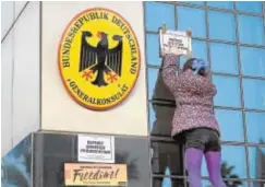  ?? AFP ?? Una manifestan­te pega un cartel en el consulado alemán en Barcelona
