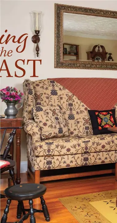  ??  ?? Joyce and Allen Foster’s living room is layered with harmonizin­g textiles accented with punch-needle pillows and dashes of brick red. A raised dough box stands in as a coffee table to help center the seating arrangemen­t. Prairie curtains and a painted floorcloth lend primitive style, while the mirror and open-leg furnishing­s visually enlarge the cozy space.