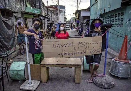 ??  ?? b À Manille, le 20 mars. Trois personnes gardent la barricade qu’elles ont elles-mêmes montée à l’entrée de leur quartier pour empêcher des personnes infectées de traverser leur zone d’habitation. Sur le carton, elles ont écrit en tagalog: “Rumeurs corona. Les ragots sont interdits ici. Ils sont contagieux”.