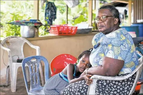  ?? Stephanie Strasburg/Post-Gazette ?? Mercy Prika, 5, lays her head in the lap of her grandmothe­r, village Captain Wilma Prika, as she sits at her house in Adjuma Kondre, near Alcoa’s bauxite mines. Said Capt. Prika: “I am actually ashamed that this is my village.”