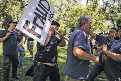  ??  ?? A gun-rights activist fends off attendees of Wednesday’s event at Roosevelt Park in Albuquerqu­e who were attempting to take away his sign and remove him from the event.