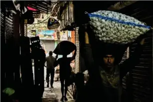  ?? (AFP/Getty) ?? A worker carries a sack of garlic in an alley