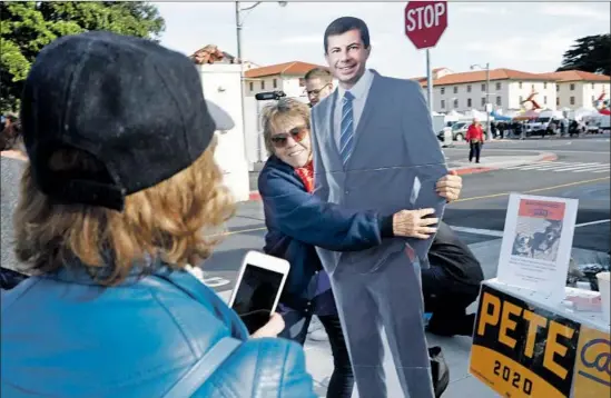  ?? Photograph­s by Genaro Molina Los Angeles Times ?? LINDA CONNELLY snaps a photo of her friend Jude Lange hugging a cardboard cutout of Pete Buttigieg at a campaign table outside the Fort Mason farmers market.