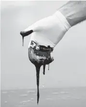  ?? GERALD HERBERT/THE ASSOCIATED PRESS FILES ?? A member of Louisiana Gov. Bobby Jindal’s staff pulls his hand out of a thick layer of oil on the surface of Barataria Bay in Plaquemine­s Parish, La., in this June 2010 photo.