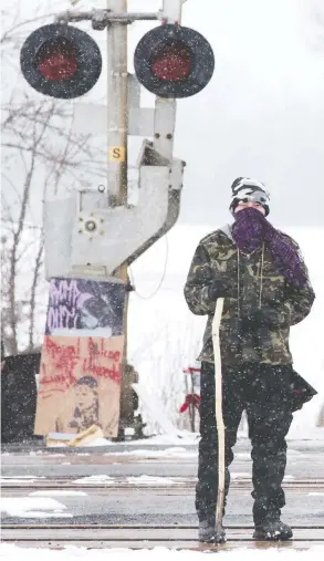  ?? LARS HAGBERG / THE CANADIAN PRESS ?? A protester stands on the closed train tracks in Tyendinaga Mohawk Territory, near Belleville, Ont., on Thursday. The blockade is in solidarity with the Wet’suwet’en
hereditary chiefs opposed to the LNG pipeline in northern British Columbia.