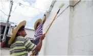  ??  ?? Juan Carlos Martes y Rigoberto Pérez pintan de blanco la fachada de su vivienda.