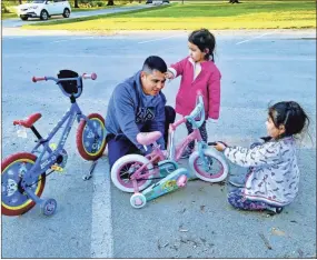  ??  ?? Argenes Argueta gets bikes ready for his daughters Andrea and Anayeli to ride at Palmer Memorial Park.