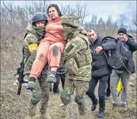  ?? ?? A woman carried by Ukrainian soldiers crosses a path while fleeing the town of Irpin and the burnt out remains of a building destroyed by Russian army shelling in the second largest Ukrainian city of Kharkiv, on Sunday.