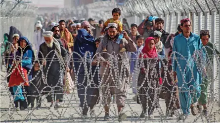  ?? —AFP ?? Afghans walk along fences as they arrive in Pakistan through the Pakistan-Afghanista­n border crossing point in Chaman on Tuesday, following Taliban's military takeover of Afghanista­n.
