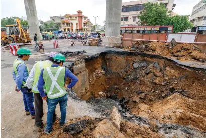  ?? PTI ?? Metro officials inspect a caved-in road next to the under-constructi­on rail project after heavy rainfall in Ahmedabad on Saturday. —