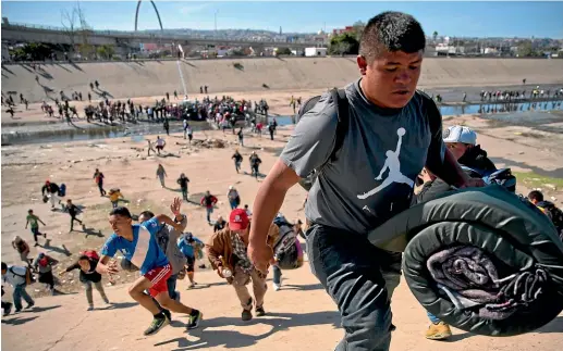  ?? AP ?? Migrants move up a riverbank at the Mexico-US border after getting past a line of Mexican police at the Chaparral border crossing in Tijuana.